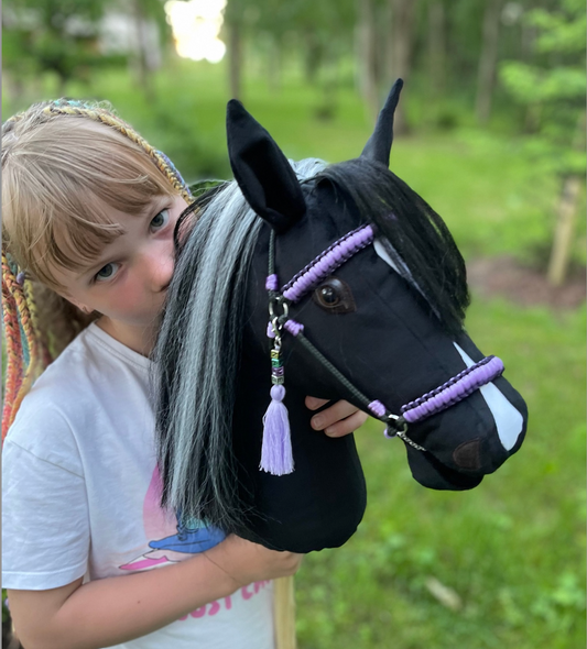 Girl holding a handmade black hobby horse with a white marking and bridle