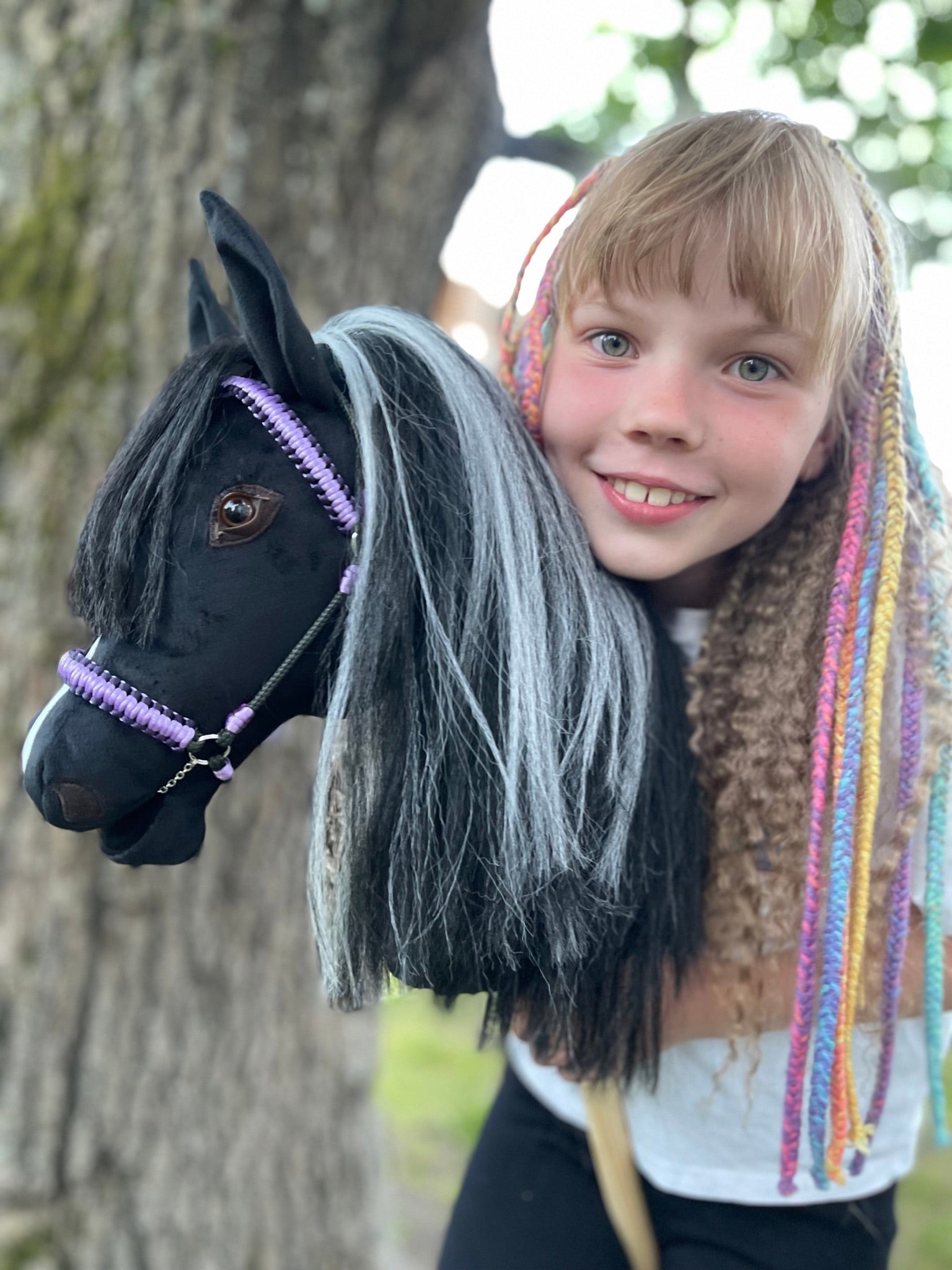 Happy girl playing with handmade black stick horse with violet bridle
