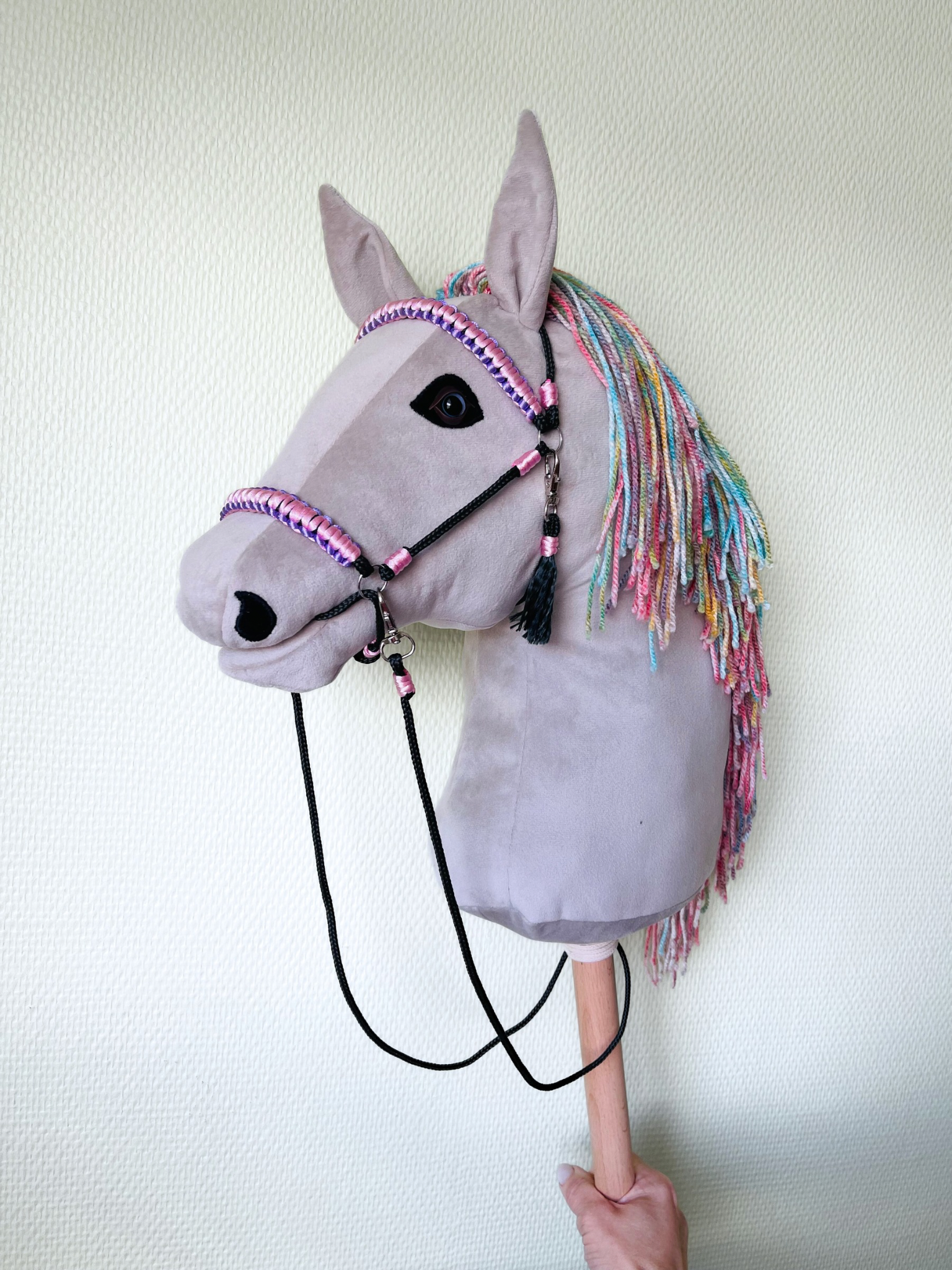 Light gray handmade hobby horse with rainbow mane and pink bridle, stick horse toy for kids and hobby horsing.