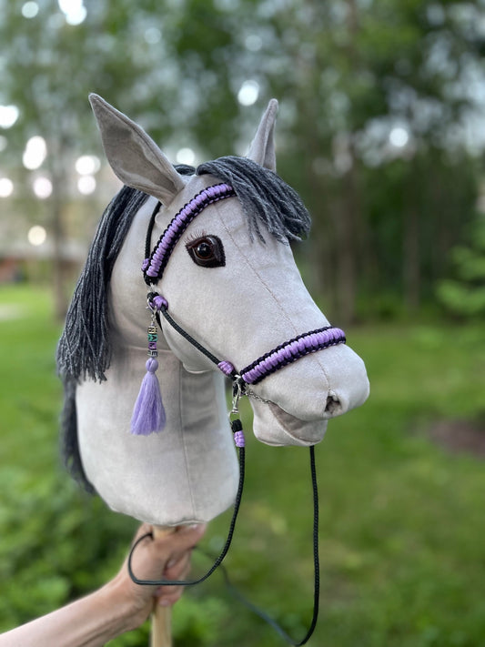 Light grey hobby horse with dark grey mane, shown with braided handmade bridle and personalized tassel name tag. Stick horse toy, handcrafted and ready for pretend play or gift-giving.