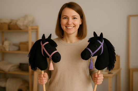 Woman smiling while holding two handmade hobby horses in a cozy workshop