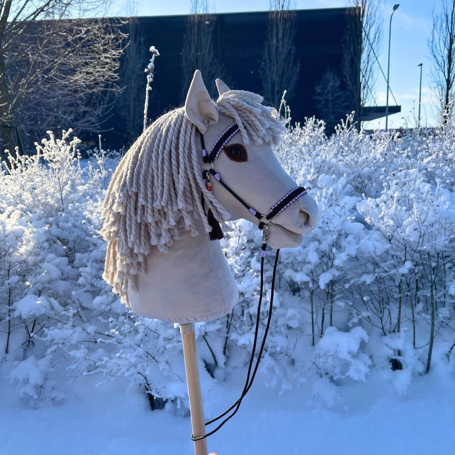 Handmade ivory hobby horse with thick yarn mane on snowy background
