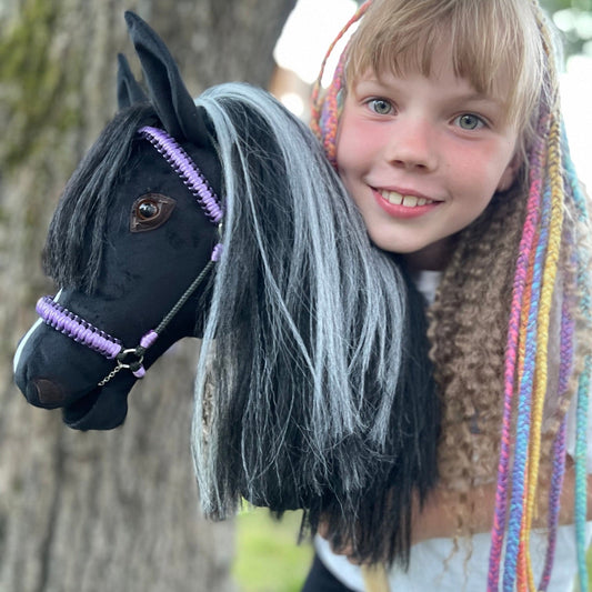 Happy girl playing with handmade black stick horse with violet bridle