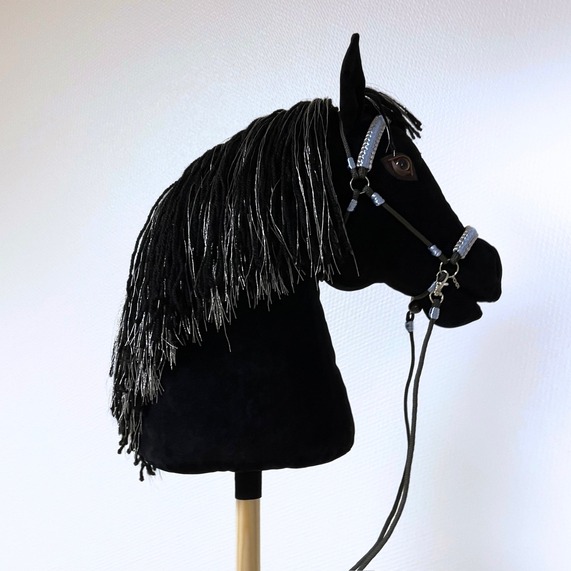 Black hobby horse with silver-threaded mane and light blue bridle, handmade stick horse with personalized pendant.