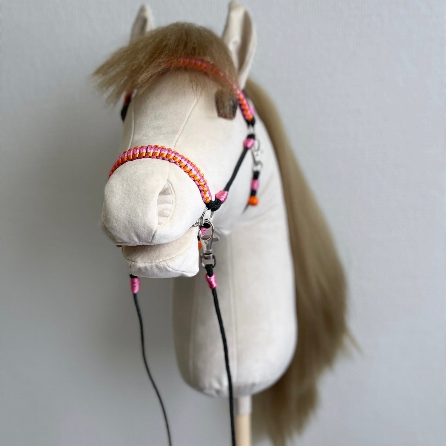 Handmade beige hobby horse with realistic faux hair mane, sunset pink bridle, reins, and personalized name tag.