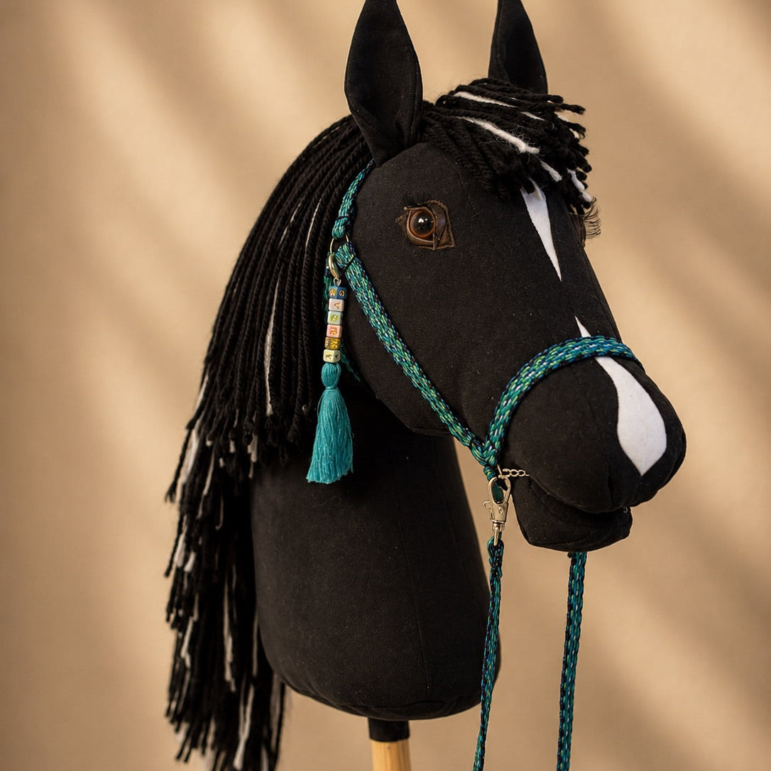 Side view of handmade black hobby horse with realistic yarn mane and turquoise hobby horse accessories