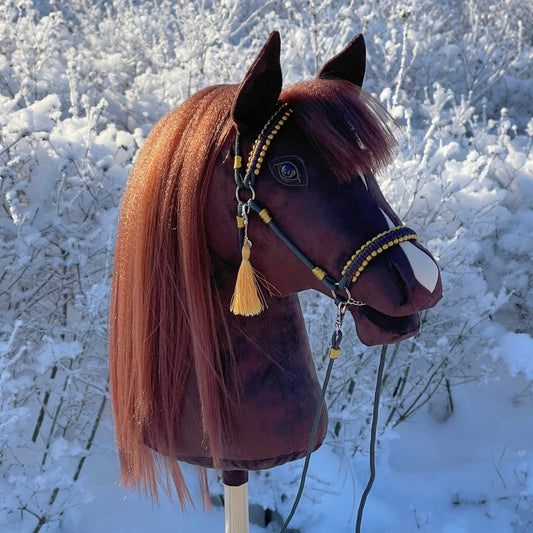 Bella dark brown handmade hobby horse with white blaze and golden bridle, side profile in snowy outdoor setting