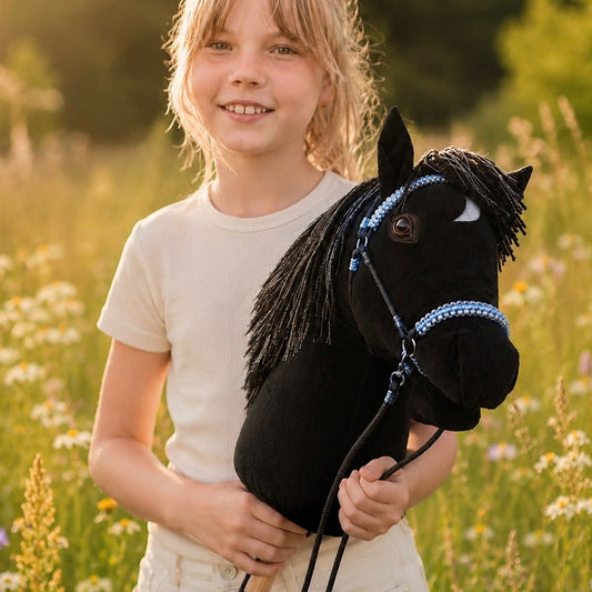 Smiling girl holding a handmade black hobby horse with a distinctive white crescent marking on its forehead, premium stick horse toy photographed outdoors in a natural setting, perfect for imaginative play and hobby horsing adventures