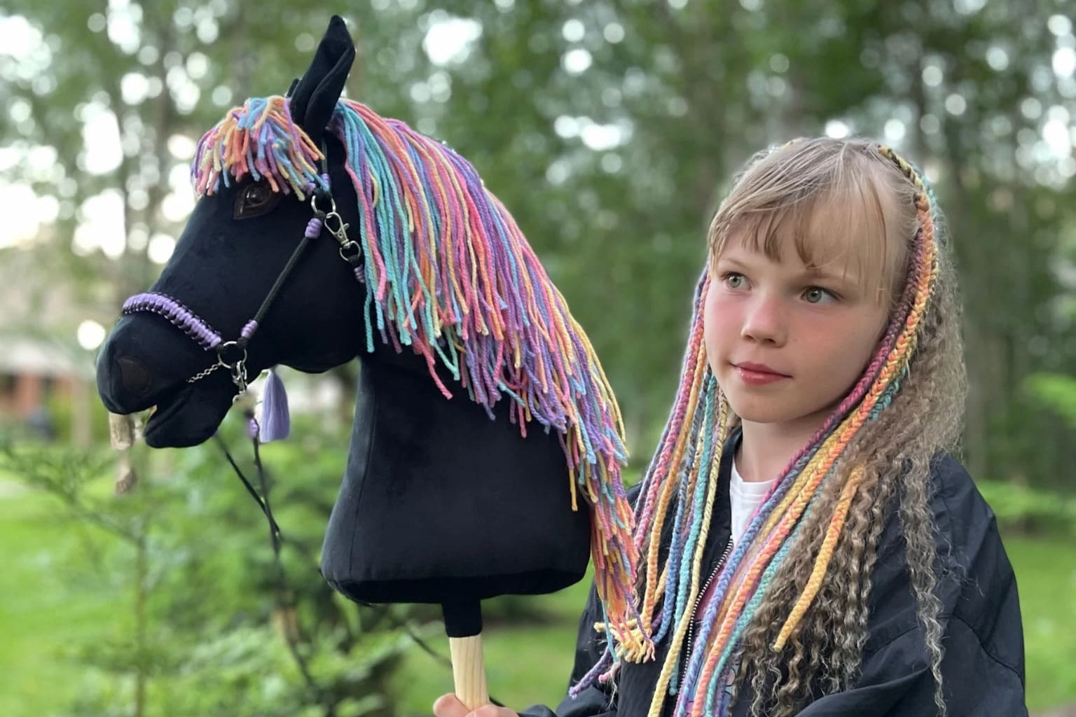 Smiling girl holding a handmade rainbow hobby horse toy with colorful mane – unique handcrafted kids gift.