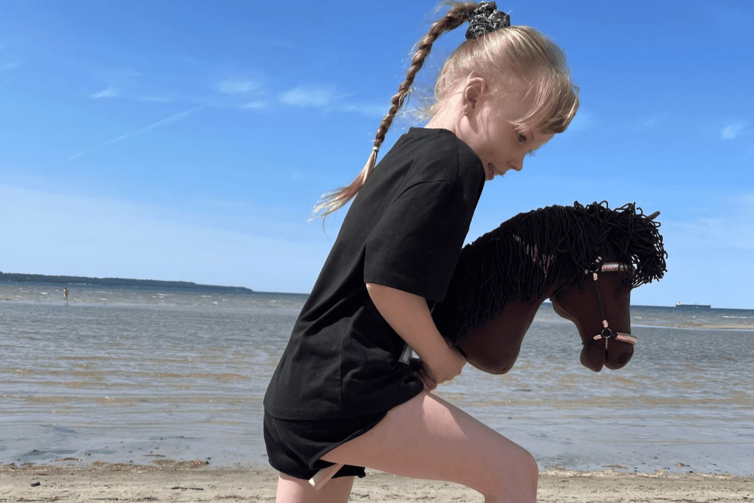 Happy girl riding a handmade brown hobby horse toy outdoors – realistic handcrafted horse for kids.