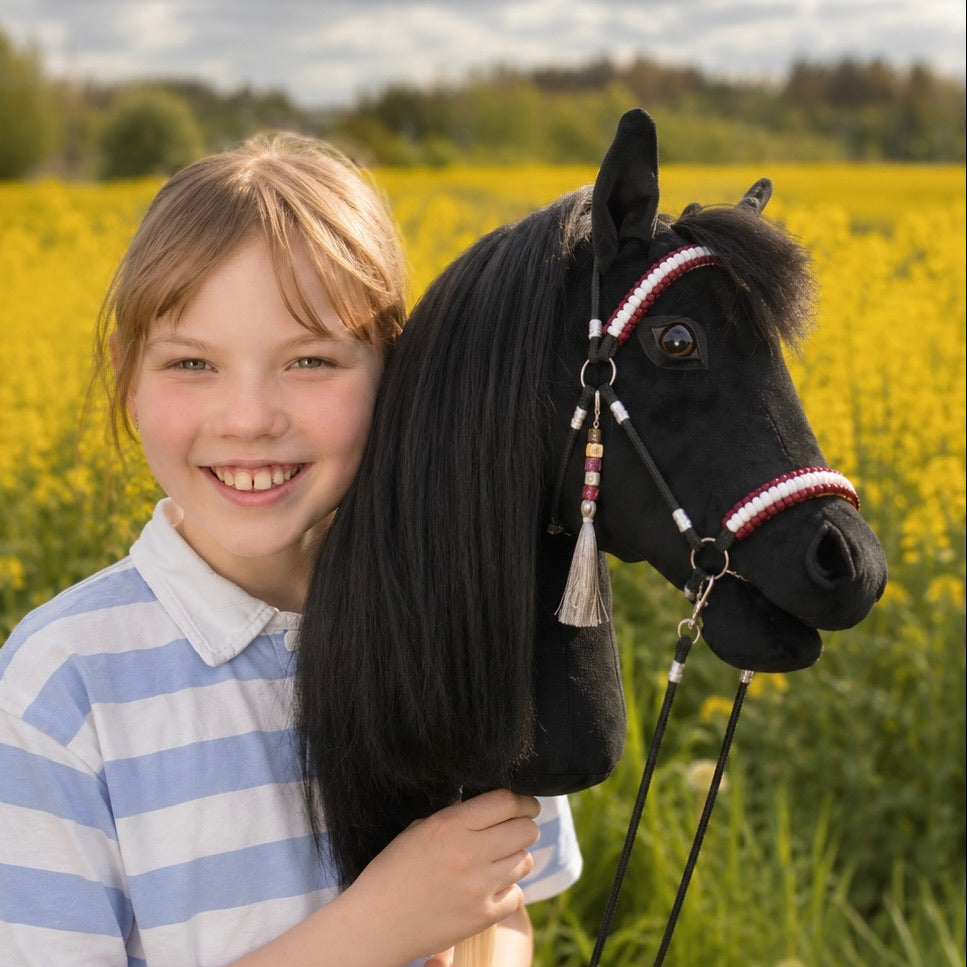 Smiling girl holding realistic black hobby horse with hair mane outdoors