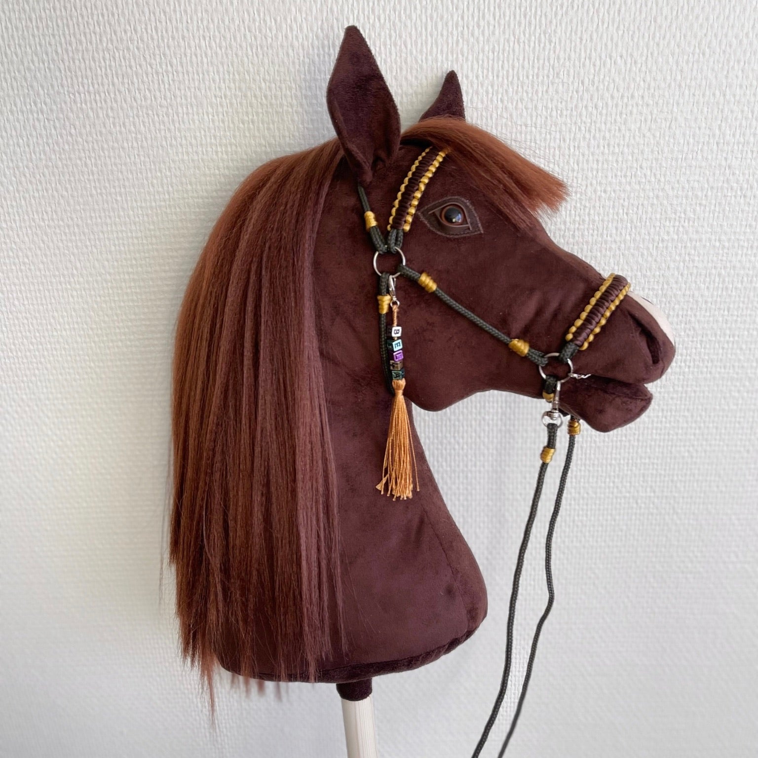 Bella handmade stick horse with realistic dark brown mane and decorative bridle, side view against neutral wall